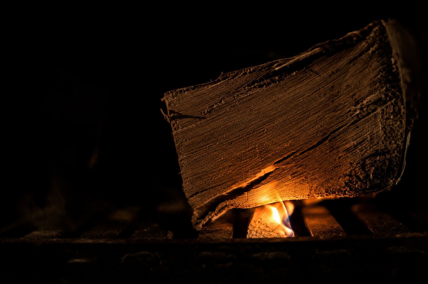 A dry split log on a stove grate, a small flame from a firelighter just taking hold along its edge
