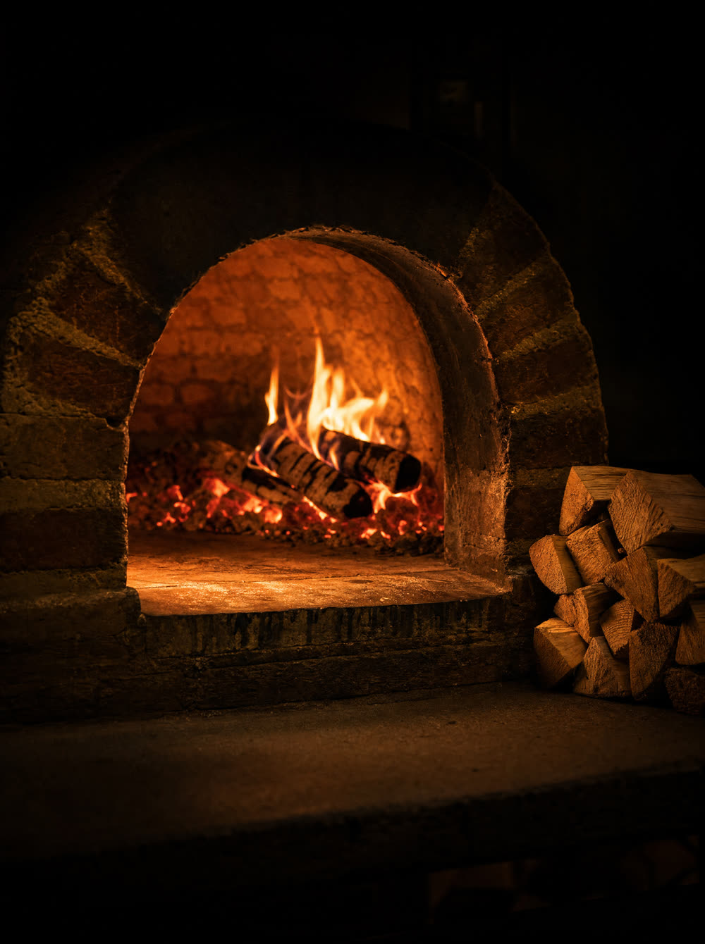 Split hardwood logs burning inside the brick dome of a wood-fired oven
